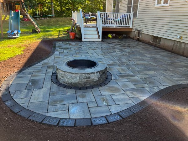 Round stone fire pit on a light gray paver patio below a deck in Middletown, CT