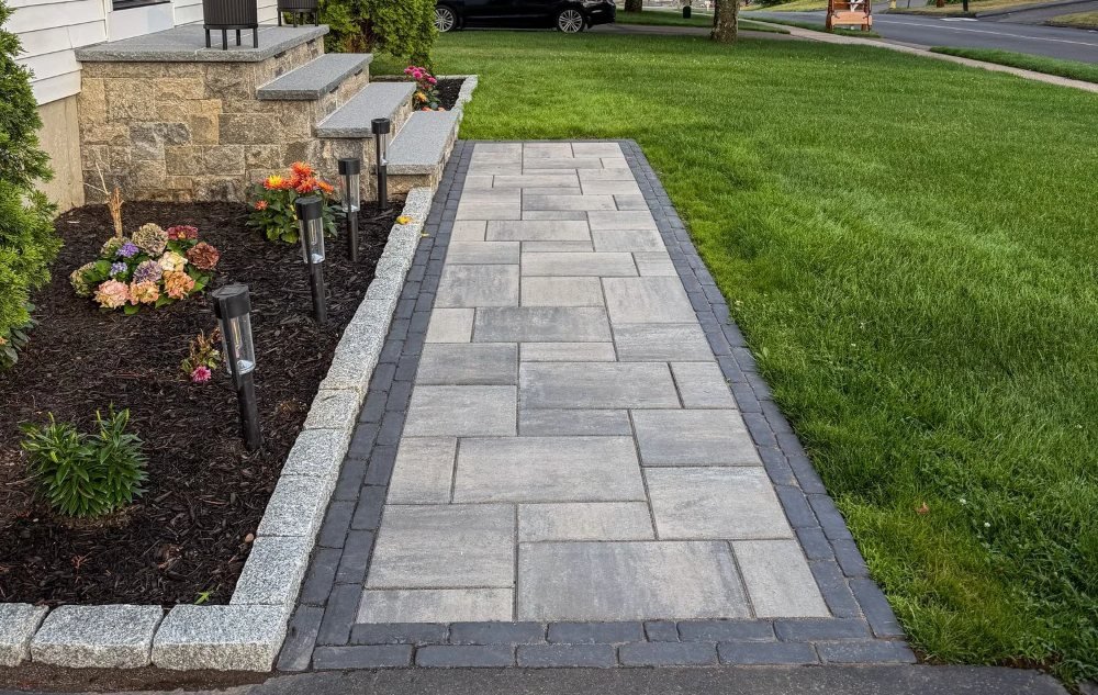 Paver front walkway with a dark border and granite cobblestone edge