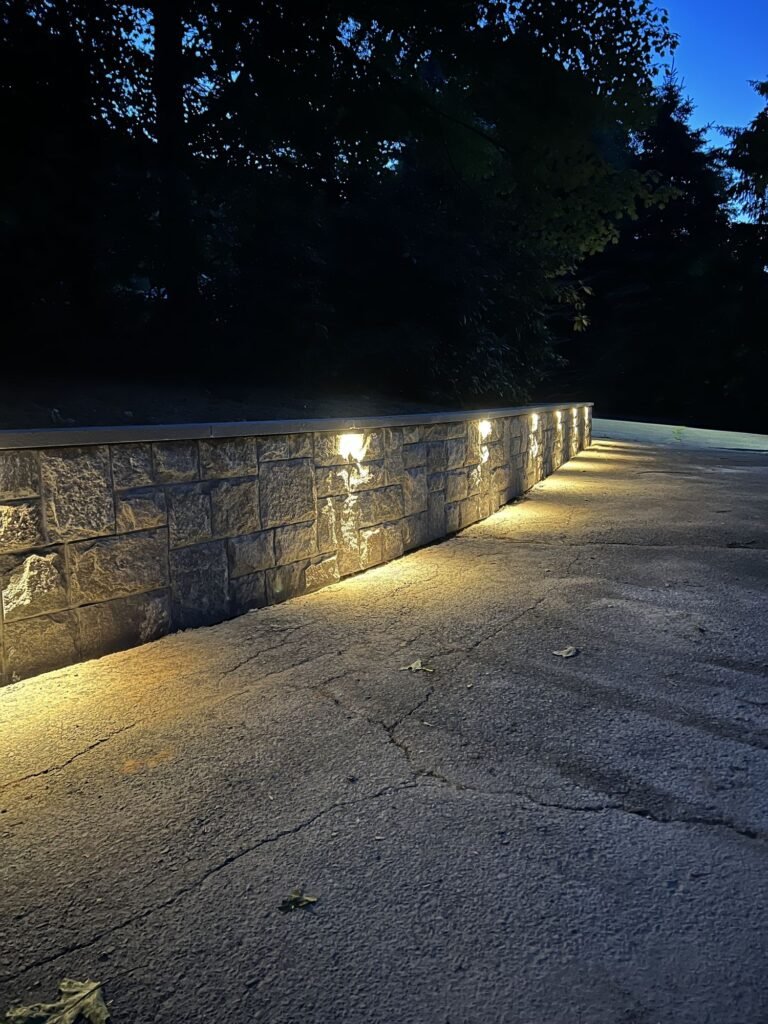 Stone-faced retaining wall with cap lights along a driveway at night in Southington, CT