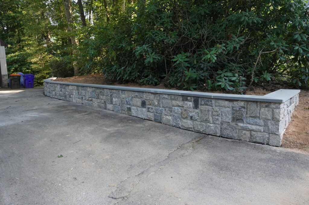 Natural stone veneer retaining wall with bluestone caps along a driveway